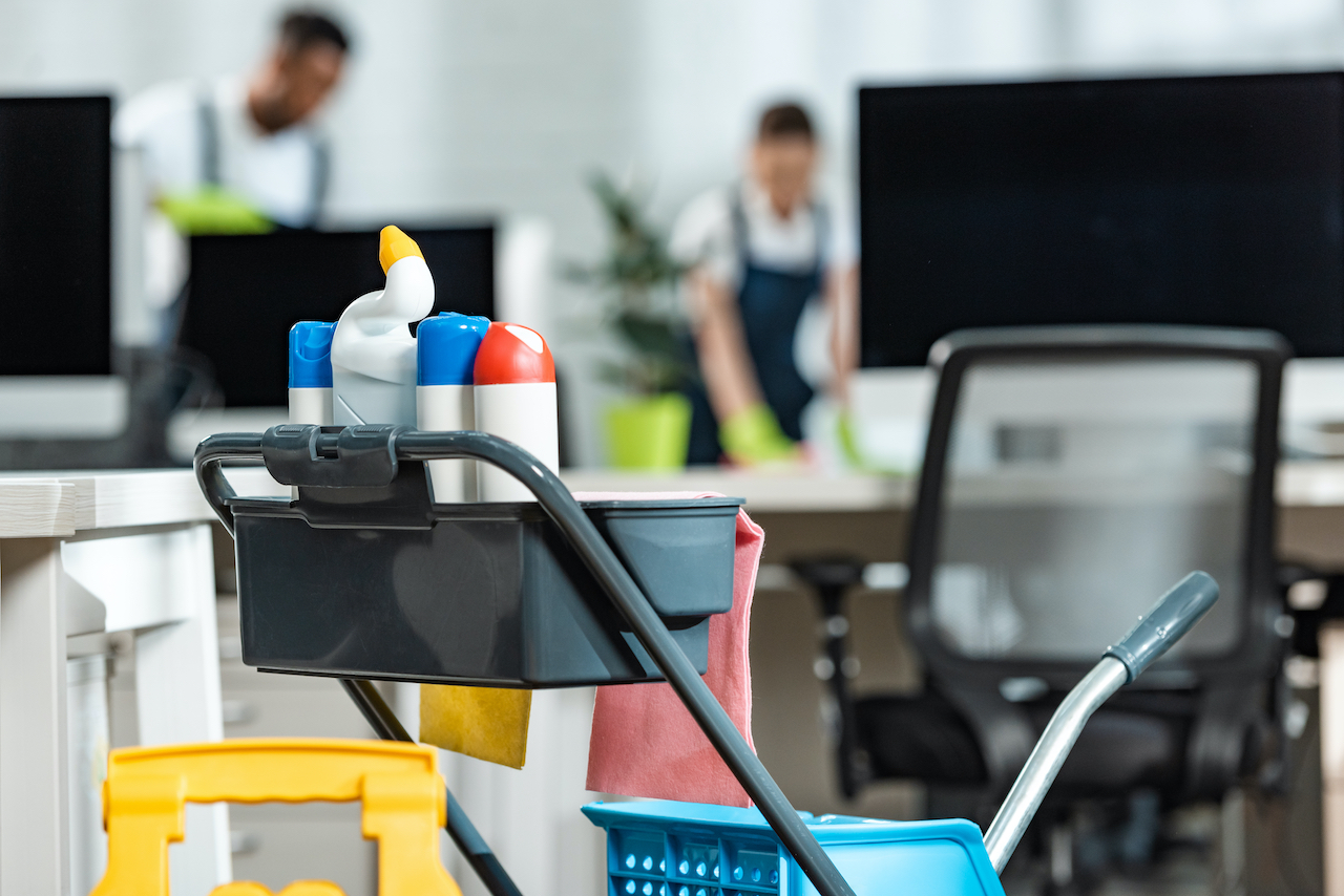 selective focus of cart with cleaning supplies and two cleaners on background